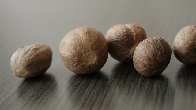 Myristica fragrans pieces collection shallow DOF slow pan 4K 2160p 30fps UltraHD footage - Assorted nutmeg fruit spice on wooden table 3840X2160 UHD panning video 