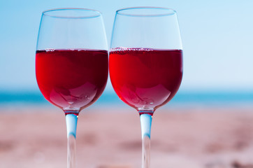 Romantic picnic with glasses of red rose wine on the beach at the summer sunny day. Sea on the background