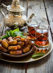 Tea with mint in arab style and dates on wooden table.