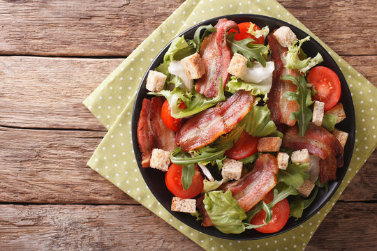 Salad of fried bacon, tomato, croutons and lettuce close-up on a plate. Horizontal top view