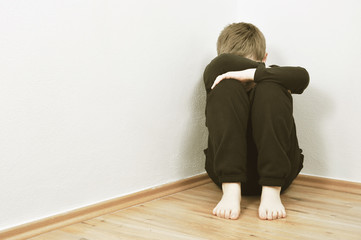 Small abused boy crying in the corner of his home because of domestic violence