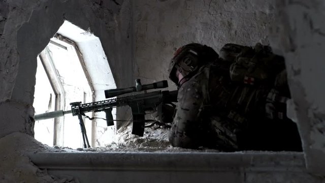 Military man with arms lies in ambush in an abandoned building