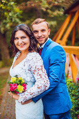 Happy bride and groom near wooden wall in the park at the wedding day walk and kiss each other.