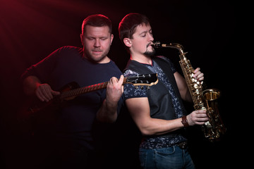 Naklejka premium Bearded guitarist with an electric guitar and a saxophonist with a saxophone playfully inspired, isolated on a black background
