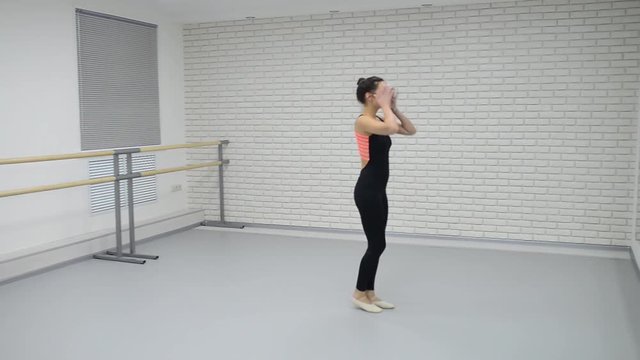 Beautiful woman in black bodysuit enter into dance studio and start dancing ballet looking at mirror