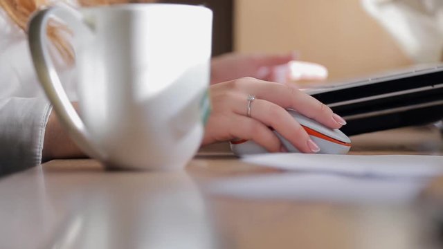 Charming woman works at personal computer, close up. Beautiful female is dressed in white daily cotton shirt with gentle french manicure. She sits down to white table. On the right side lie alabaster