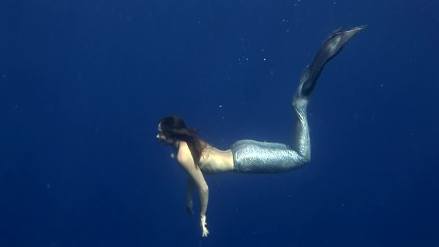 Young girl model underwater seamaiden costume on blue background in Red Sea. Filming a movie at camera. Extreme sport in marine landscape, coral reefs, ocean inhabitants.