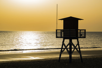 Sunset over a beach with a rescue post