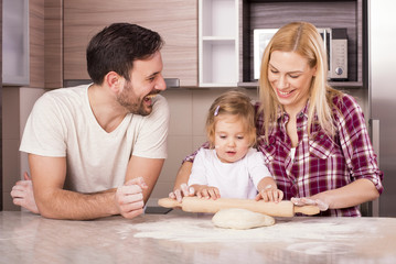 Fototapeta premium Young couple with kid having fun in the kitchen while making fresh dough