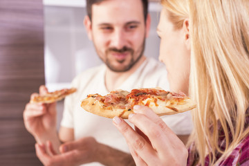 Couple having fun in the kitchen while making and eating pizza