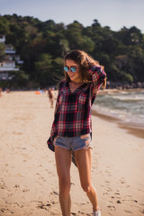 Summer sunny lifestyle fashion portrait of young stylish hipster woman walking on beach,wearing cute trendy outfit, travel, hikes, smiling enjoy her weekends