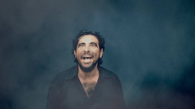 An angry man, believing to be a werewolf, in a thick fog. Medium shot.
