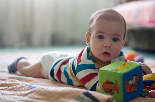 Cute little baby with big brown beautiful eyes laying on floor with kids colorful toys.Candid image of young baby playing at home/Little baby play with toys on the floor