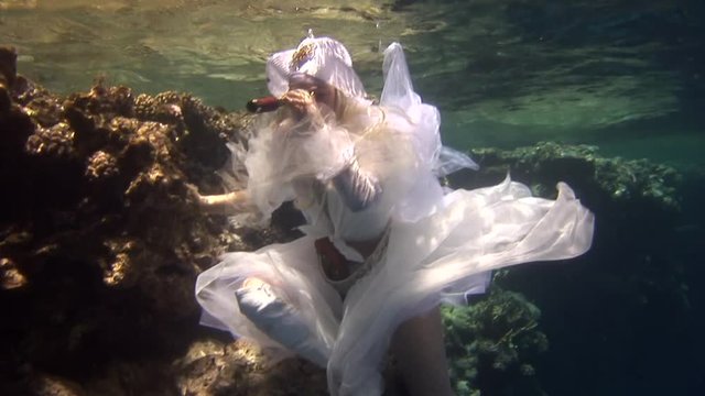 Underwater model free diver in costume pirate swims in clean water in Red Sea. Filming a movie. Young girl smiling at camera. Extreme sport in marine landscape, coral reefs, ocean inhabitants.