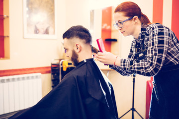 female hairdresser is cutting hair of bearded man client