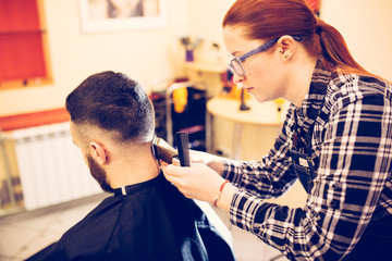 Fototapeta premium female hairdresser is cutting hair of bearded man client