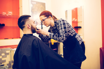 Fototapeta premium female hairdresser is cutting hair of bearded man client