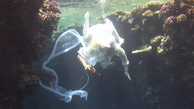 Underwater model free diver in costume pirate swims in clean water in Red Sea. Filming a movie. Young girl smiling at camera. Marine landscape, coral reefs, ocean inhabitants.
