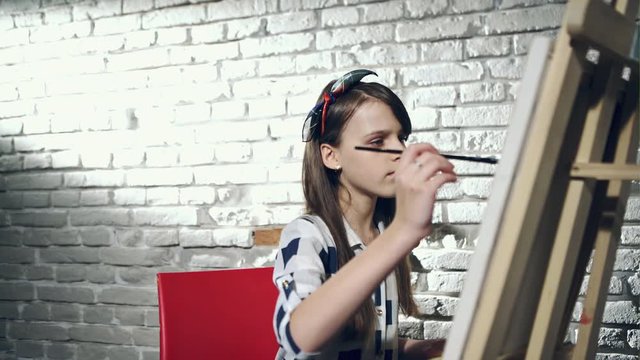Creative pensive painter child paints a colorful picture on canvas with oil colors in workshop.