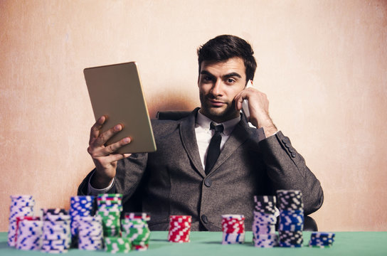 Handsome elegant poker player, online poker tablet and smartphone, poker chips on table 