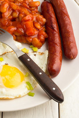 Fried eggs, beans, grilled sausages close-up on a wooden white table.