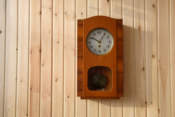 Naklejka premium Mechanical clock in a wooden case hanging on a wooden wall.
