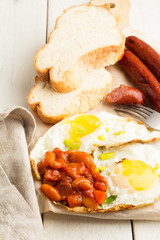 Scrambled eggs, bread, sausages, beans and fork on a cutting board on a wooden table close-up.