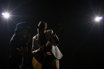 Fototapeta na wymiar Musician Duo band hand holding the microphone and singing a song and playing the guitar on black background with spot light and lens flare, musical concept