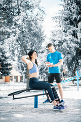 Woman doing sit ups outdoor with her trainer.