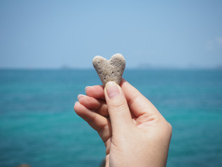 hand holding heart shape stone over summer beach background