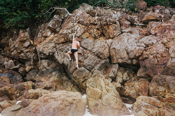 Man in beachwear clibing a rock. Back view of a man wearing swimwear Climbing on a rock. Horizontal outdoors shot.