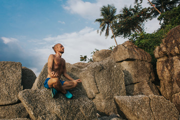 Man at rock in lotus pose. Man sitting on a huge stone in the lotus position. Horizontal outdoors shot.