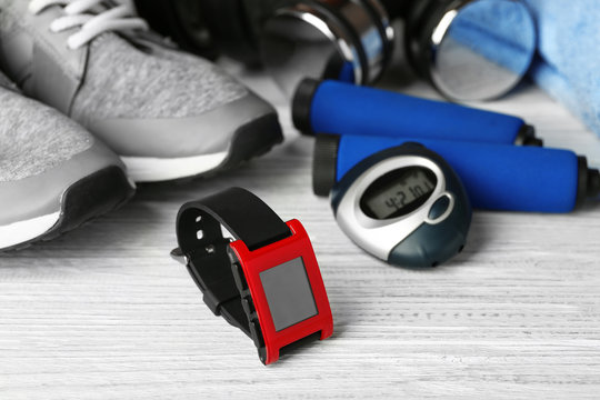 Heart rate monitor watch and sportive equipment on light wooden background