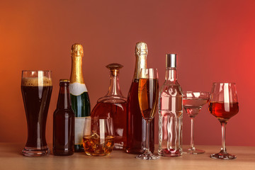Table with different bottles of wine and spirits on color background