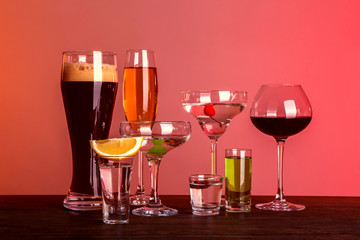 Table with glasses of wine and spirits on color background