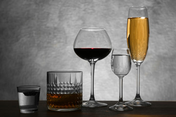 Different glasses of wine and spirits on color background