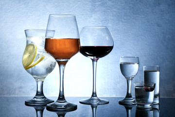 Different glasses of wine and spirits on color background