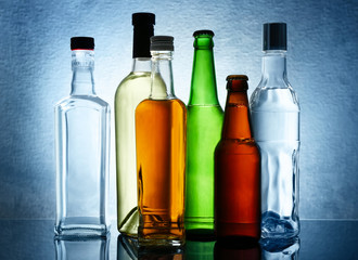 Different bottles of wine and spirits on color background