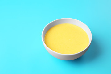 Bowl with tasty cheese sauce on color background