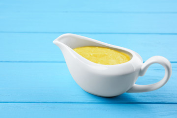 Gravy boat with tasty cheese sauce on color wooden background