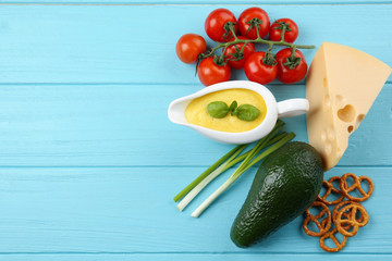 Gravy boat with cheese sauce and different products on color wooden background