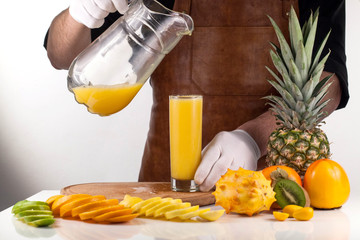 Full glass of orange juice next to assorted fruits. Man holding a jar with juice