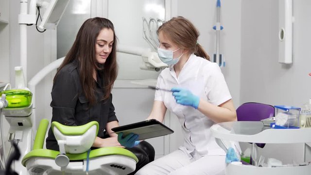 Healthy teeth and dental healthcare. Confident professional doctor dentist is showing x-ray teeth on a tablet. Female dentist in mask and lab coat.