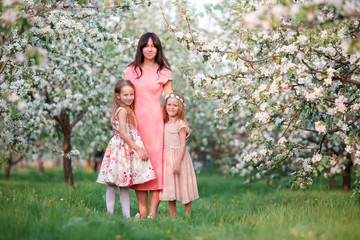 Adorable little girls with young mother in blooming cherry garden on beautiful spring day