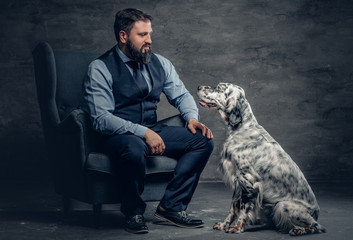 Stylish bearded male sits on a chair and the Irish setter dog.