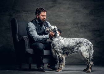 Stylish bearded male sits on a chair and the Irish setter dog.