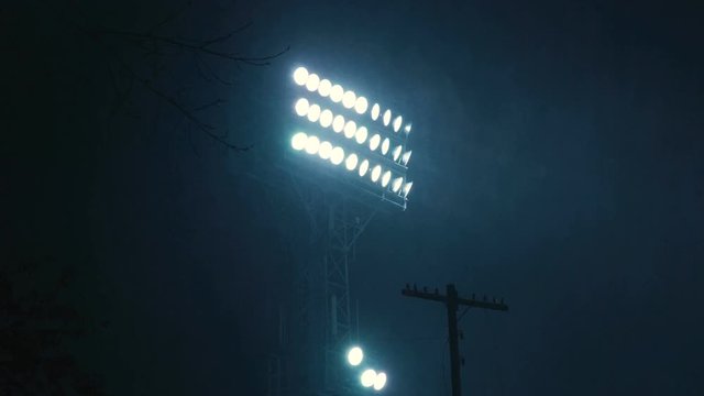 The searchlight at the stadium shines brightly in the dark. A bright light in the dark sky. Bright spotlight. A bright spotlight illuminates the sports stadium. A bright spotlight on a sports stadium