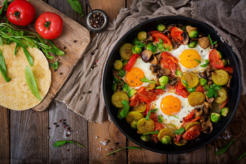 Breakfast for two. Fried eggs with vegetables - shakshuka in a frying pan on a wooden background in rustic style. Flat lay. Top view