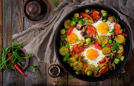 Breakfast for two. Fried eggs with vegetables - shakshuka in a frying pan on a wooden background in rustic style. Flat lay. Top view