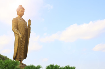 The large standing gold buddha and buddhism sacred for worship with flare and sunlight on clear...